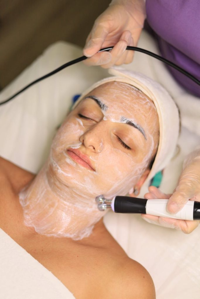 Client receiving advanced skincare treatment with facial toning device in a clinic.