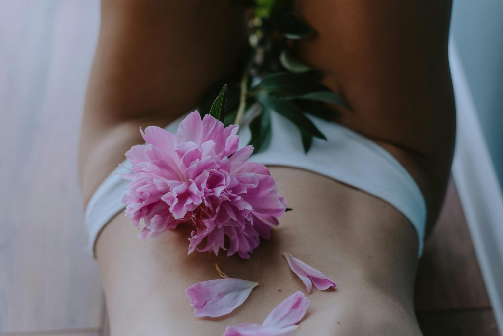 Artistic image of a woman with peony flower petals on skin, capturing sensuality and elegance.